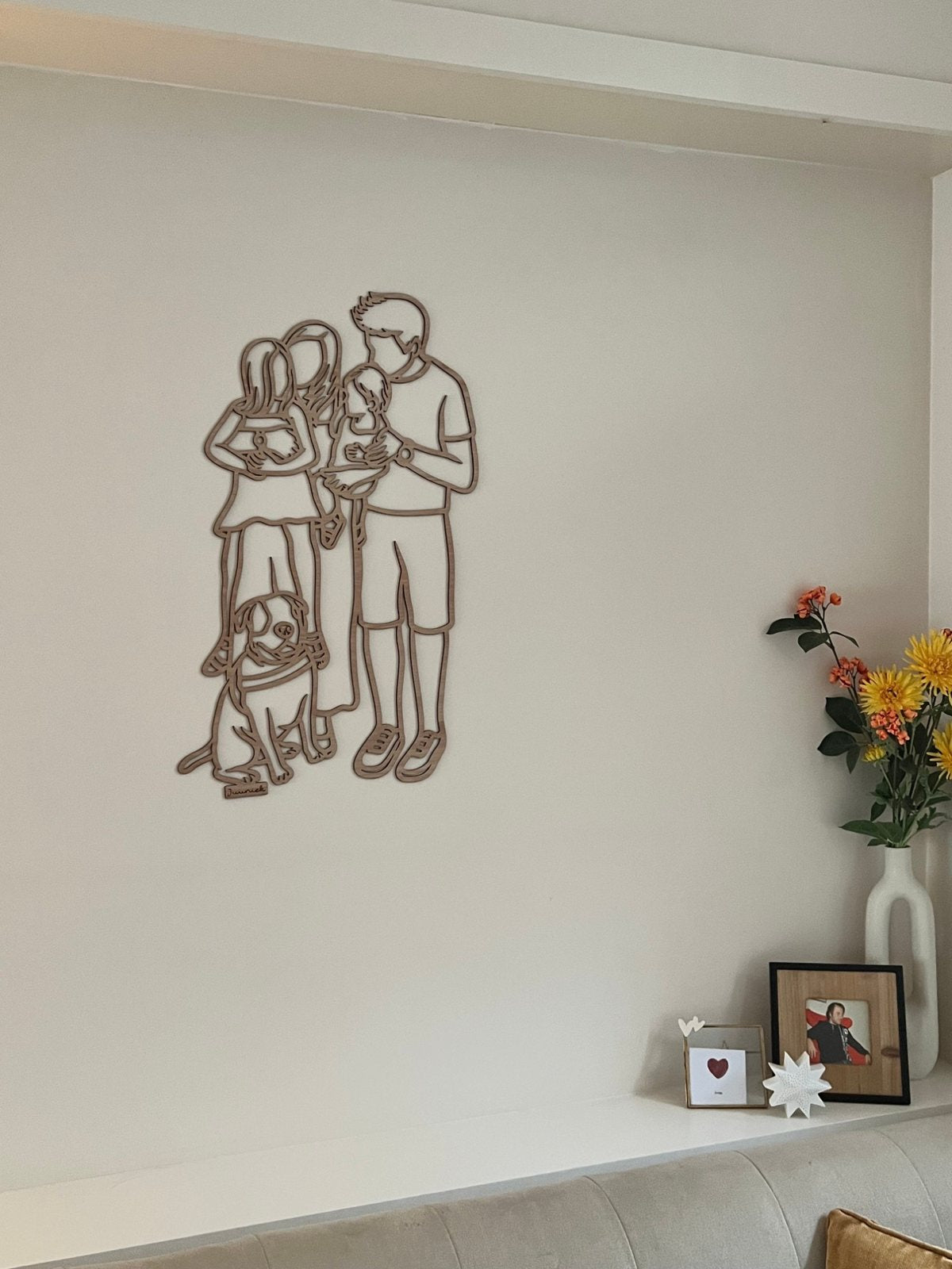 Linienporträt aus Holz einer Familie an der Wand, mit Blumen und einem kleinen Bilderrahmen darunter