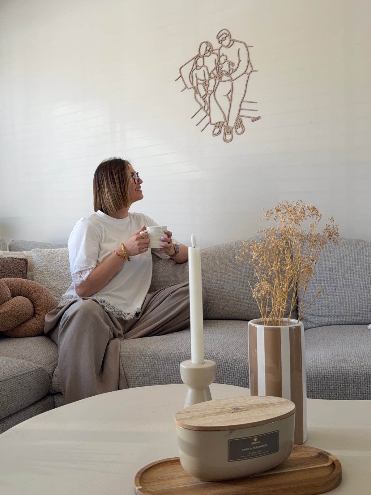 Mama auf dem Sofa betrachtet das Linienporträt aus Holz ihrer Familie an der Wand