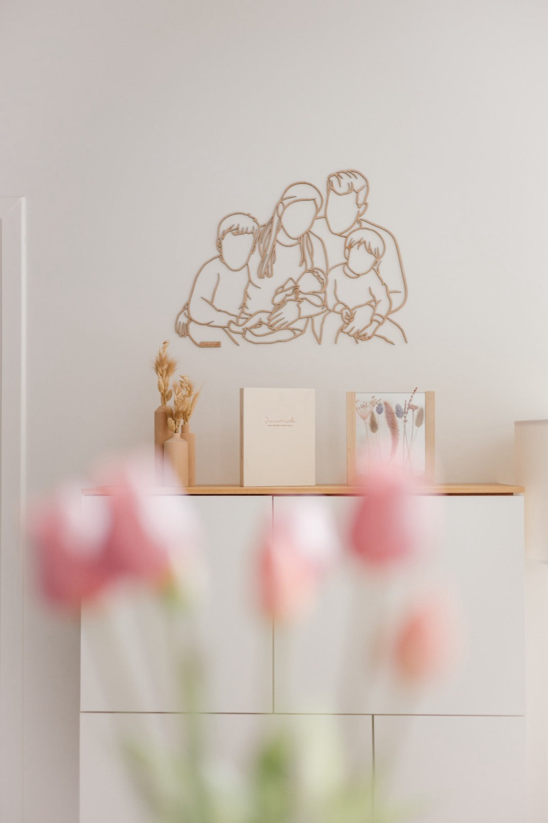 Linienporträt aus Holz von einer jungen Familie mit Baby über der Kommode